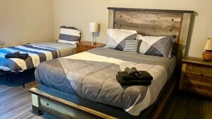 A bedroom with a large bed, a smaller bed, wooden headboard, bedside tables, and a lamp.
