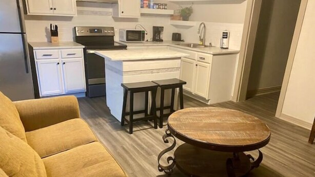 A modern kitchen with white cabinets, a central island with stools, and a round wooden table.