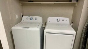 A laundry room with two stacked front-loading washing machines and a shelf above them.