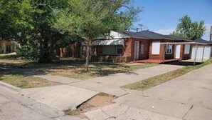 A residential property with a brick house, a detached garage, and a driveway with visible cracks.