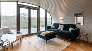 Una sala de estar moderna con una mesa de comedor de cristal, un sofá verde y un ventanal con vistas al exterior.