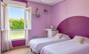 Une chambre avec deux lits, une fenêtre avec des rideaux, une table de chevet avec des livres et une petite étagère avec des objets décoratifs.