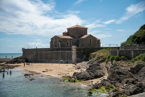 A coastal church with a stone facade, situated on a rocky shoreline with a beach in the foreground.