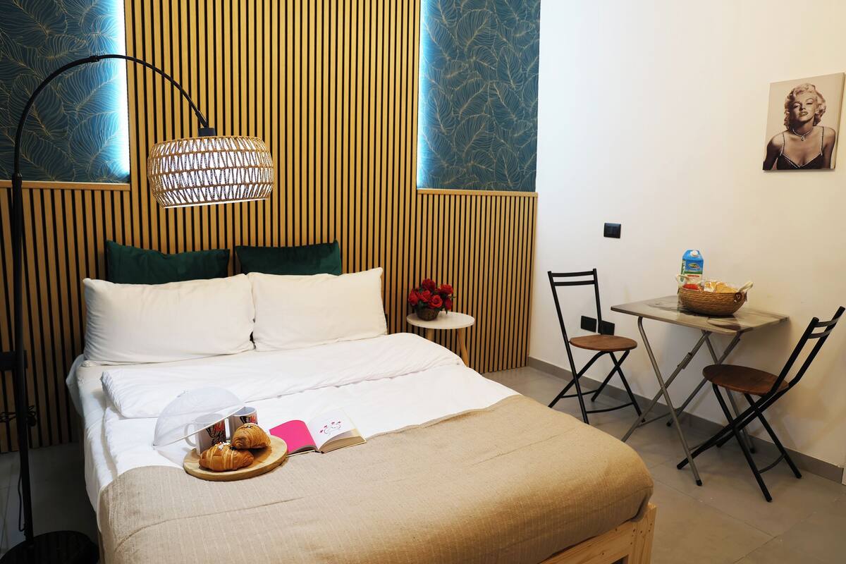 A neatly made bed with pillows, a bedside table with a basket, and a chair.