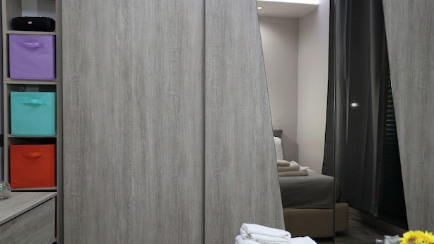 A hotel room with a grey wardrobe, a bed, and a table with towels and a flower vase. - Milly's House (Naples)