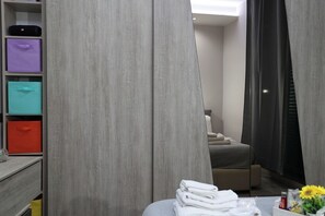Habitación de hotel con un armario gris, una cama y una mesa con toallas y un jarrón.