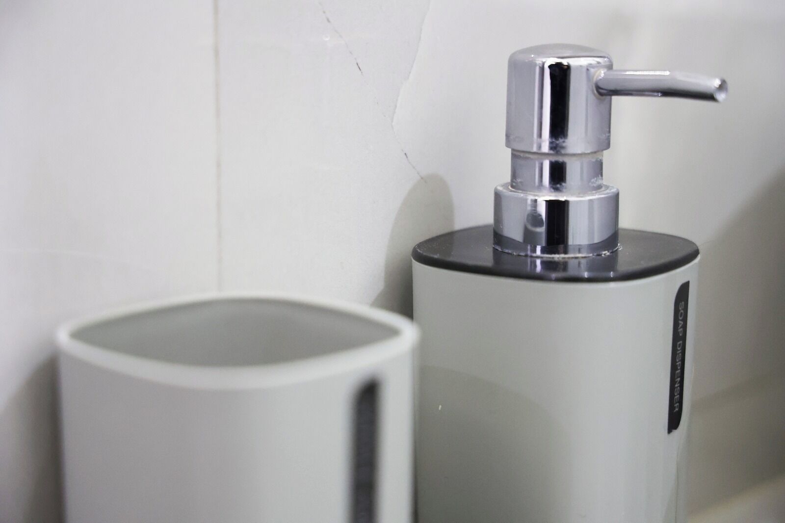 A soap dispenser and a trash can in a bathroom.