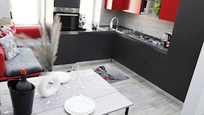 A modern kitchen with dark cabinets, a red accent wall, and a dining area with a table set for two. - Milly's House (Naples)
