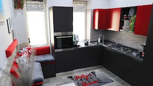 A compact kitchen with modern appliances, a dining area with a red and grey sofa, and a kitchen island. - Milly's House (Naples)
