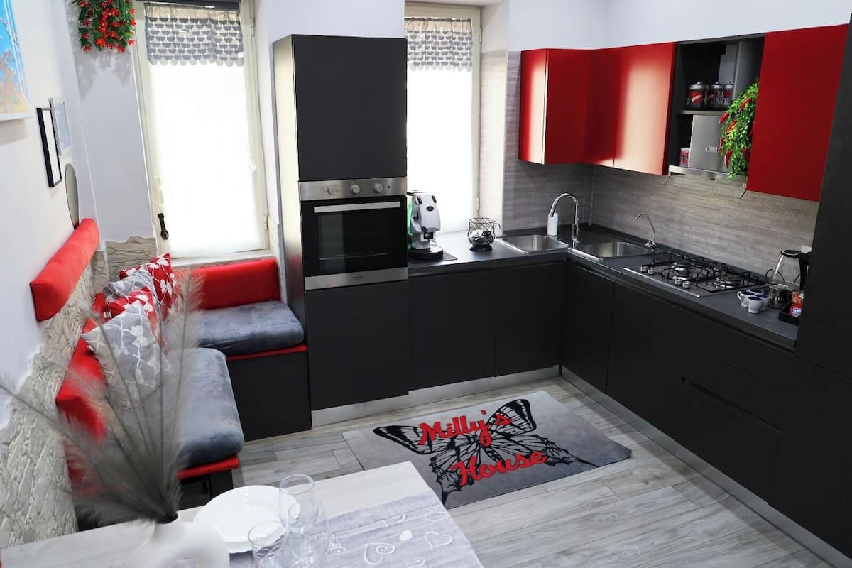 A compact kitchen with modern appliances, a dining area with a red and grey sofa, and a kitchen island.