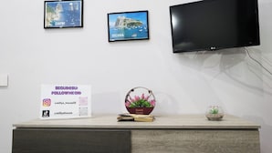 A modern room with a flat-screen TV mounted on the wall, two framed pictures of Capri and Ischia, a sign promoting social media followings, a small potted plant, and a decorative basket. - Milly's House (Naples)