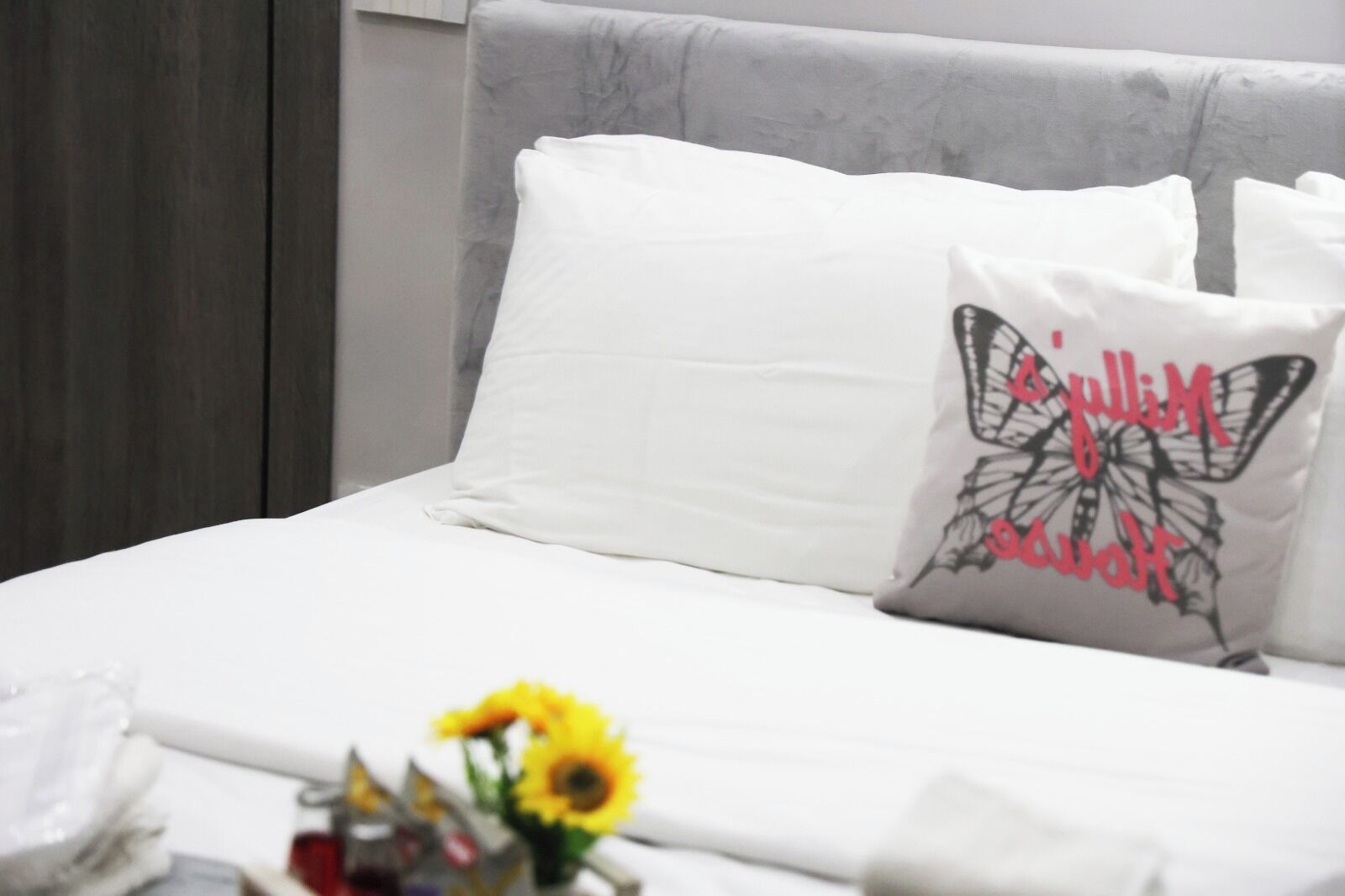 A bed with white bedding and a decorative pillow with a butterfly design.