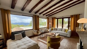A spacious room with a bed, sofa, and armchair, large windows with a view of mountains, and a pool visible through the windows. - Mas Nou CostaBravaSi - Pool, AC, nature, views (Platja d'Aro)