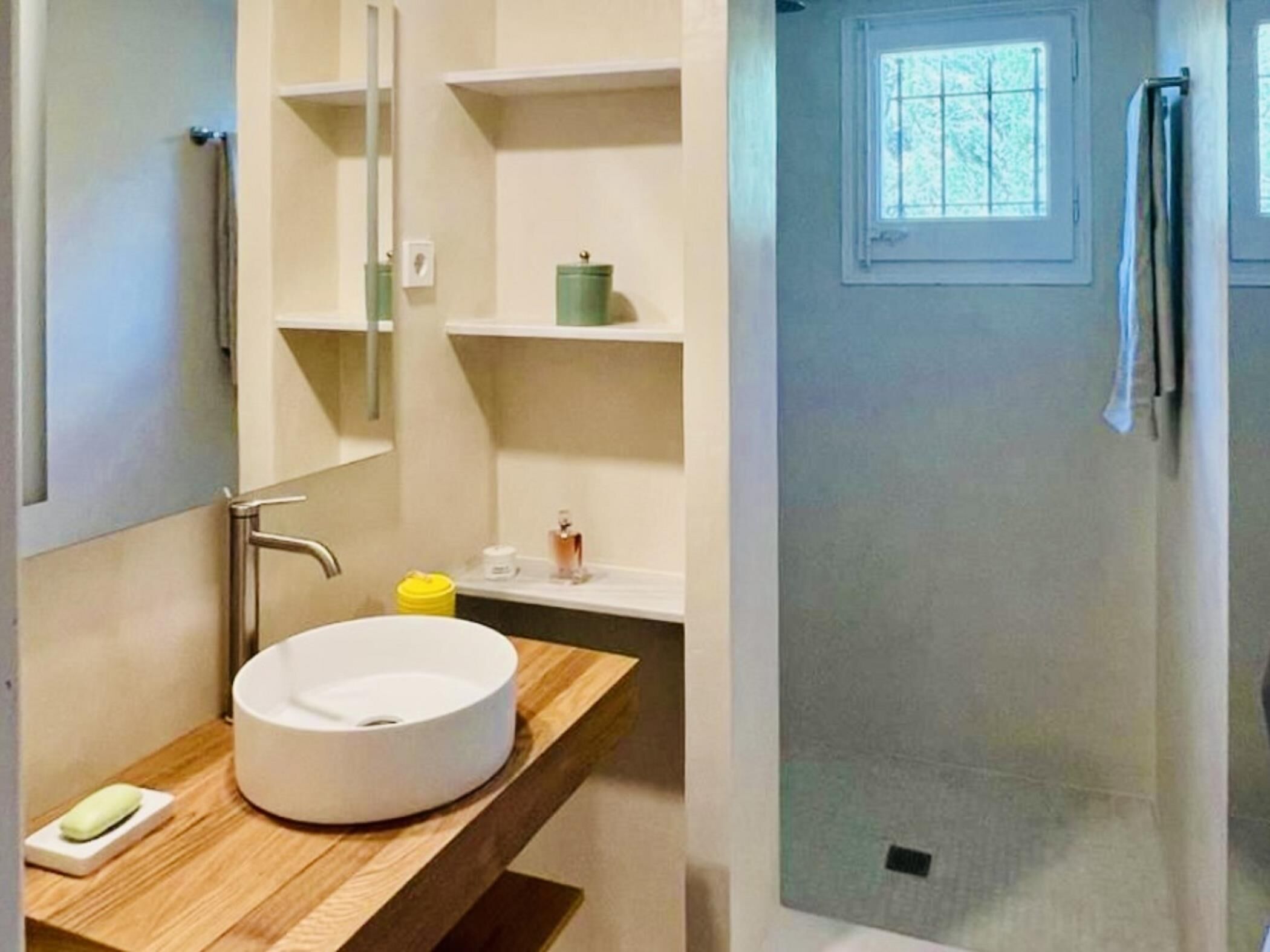 A bathroom with a wooden vanity, a round sink, a mirror, and a window.
