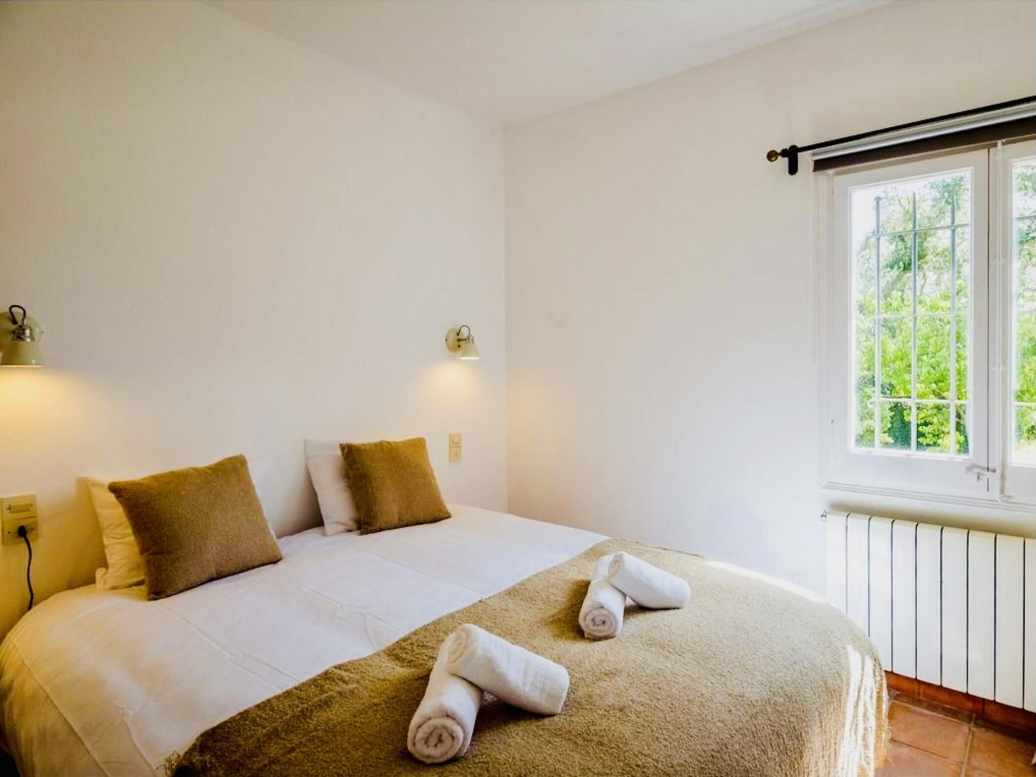 Un dormitorio con cama, dos almohadas, una ventana y un radiador.