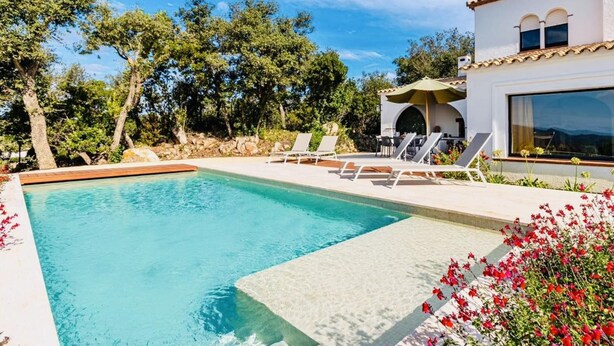 A swimming pool with lounge chairs and a patio area, surrounded by trees and a white building with large windows. - Mas Nou CostaBravaSi - Pool, AC, nature, views (Platja d'Aro)
