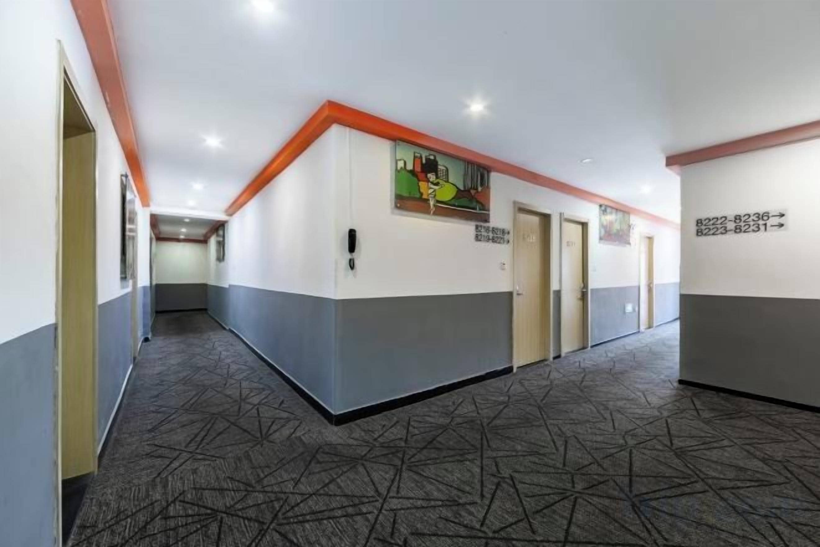 Un couloir d’hôtel avec des portes, une moquette à motifs et un mur orné de flèches indiquant les directions.