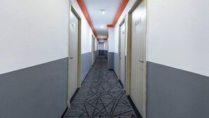 Un lungo e stretto corridoio con porte su entrambi i lati, una moquette decorata e tocchi arancioni sul soffitto e sulle pareti.