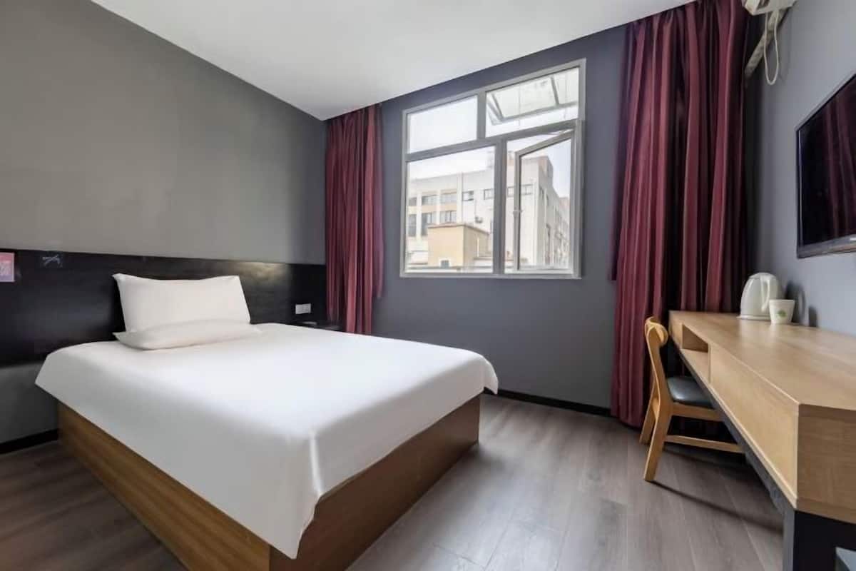 A hotel room with a bed, a desk, a chair, a window with curtains, and a television on the wall.