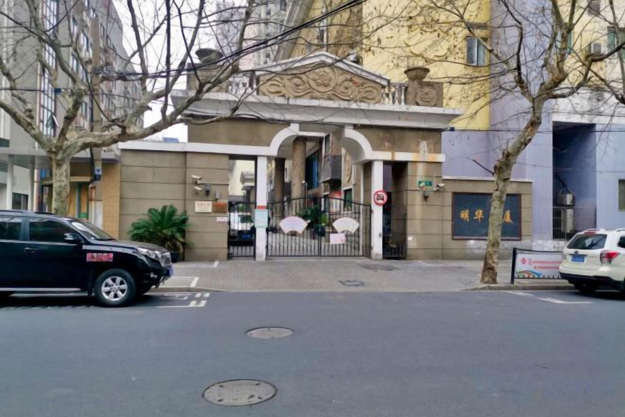 A building with a gated entrance, a manhole cover on the street, and a parked car.