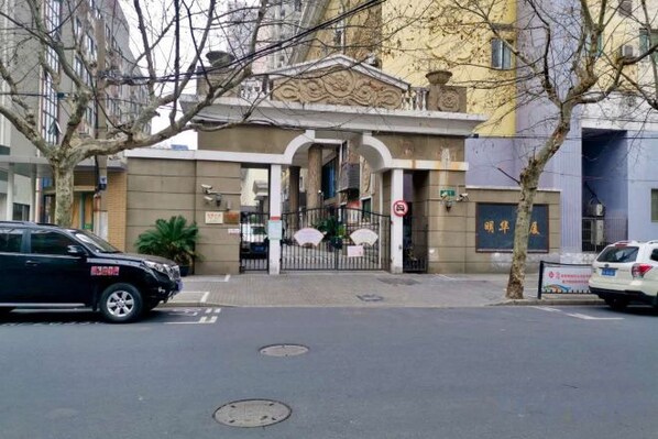 A building with a gated entrance, a manhole cover on the street, and a parked car. - Red House Hotel (Shanghai Red House Hospital Lujiabang Road Subway Station Branch) (Shanghai)