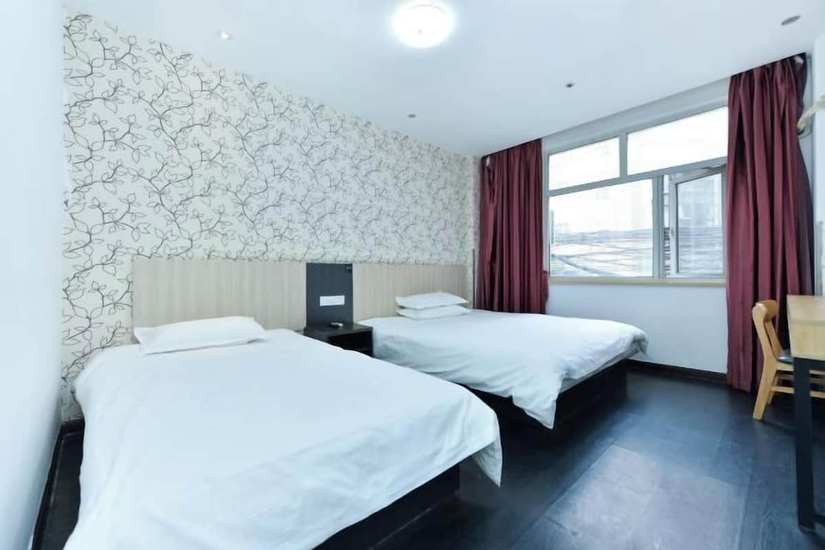A hotel room with two beds, a window with curtains, a desk, and a wall with a leaf pattern.