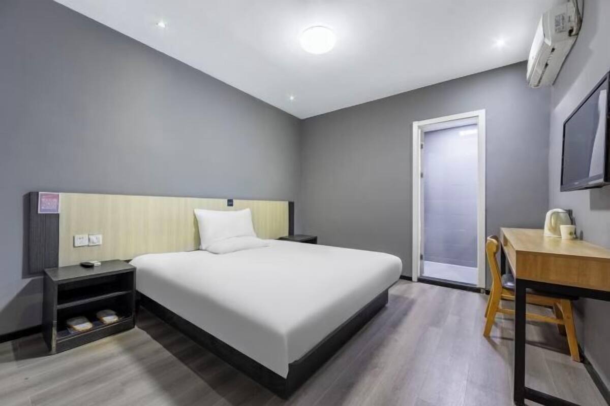 A modern hotel room with a large bed, a desk, a chair, a nightstand, and a TV.