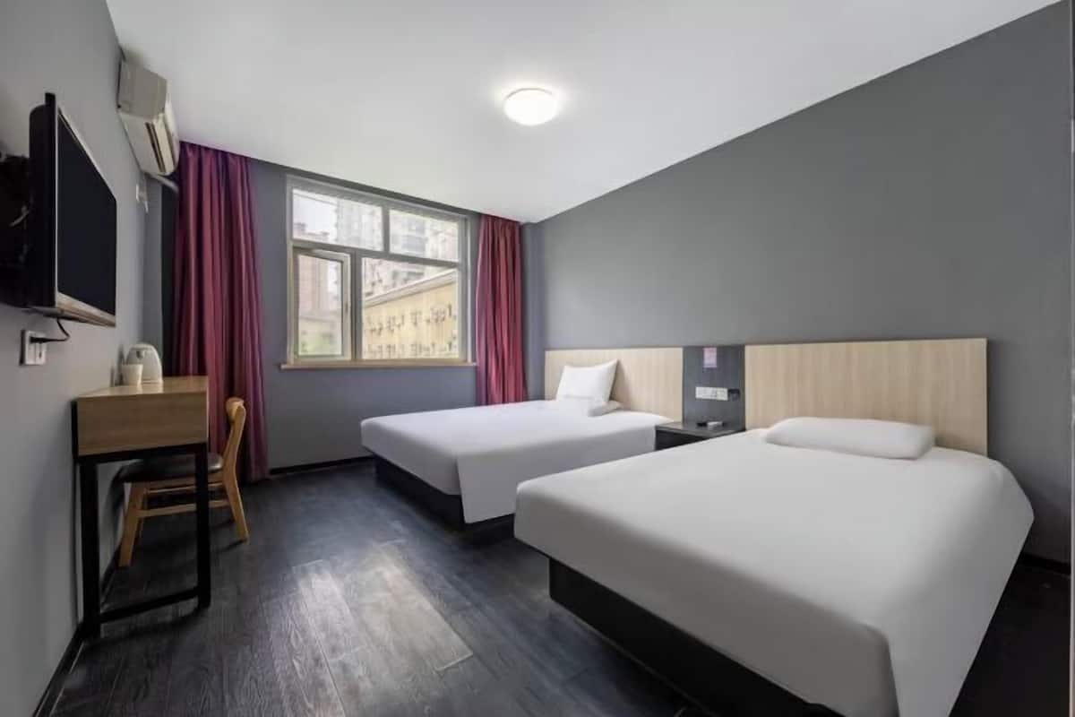 A hotel room with two beds, a desk, a chair, a TV, and a window with curtains.
