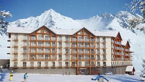 A multi-story hotel with balconies, a ski slope in front, and snow-covered mountains in the background. - New Gudauri, Redco apartments (Gudauri)