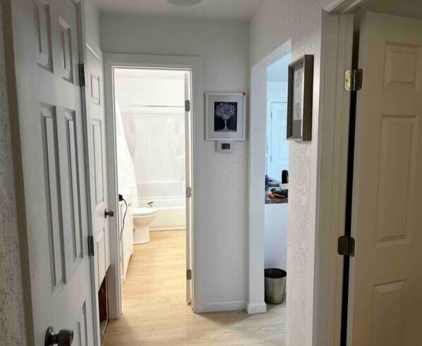 A narrow hallway with white doors on both sides, leading to a bathroom with a toilet and a shower. - Affordable + Pet Friendly 1 BR + sofa bed/1BA #B (Lubbock)