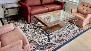 A living room with a red sofa, a glass coffee table, and two pink armchairs. - Affordable + Pet Friendly 1 BR + sofa bed/1BA #B (Lubbock)