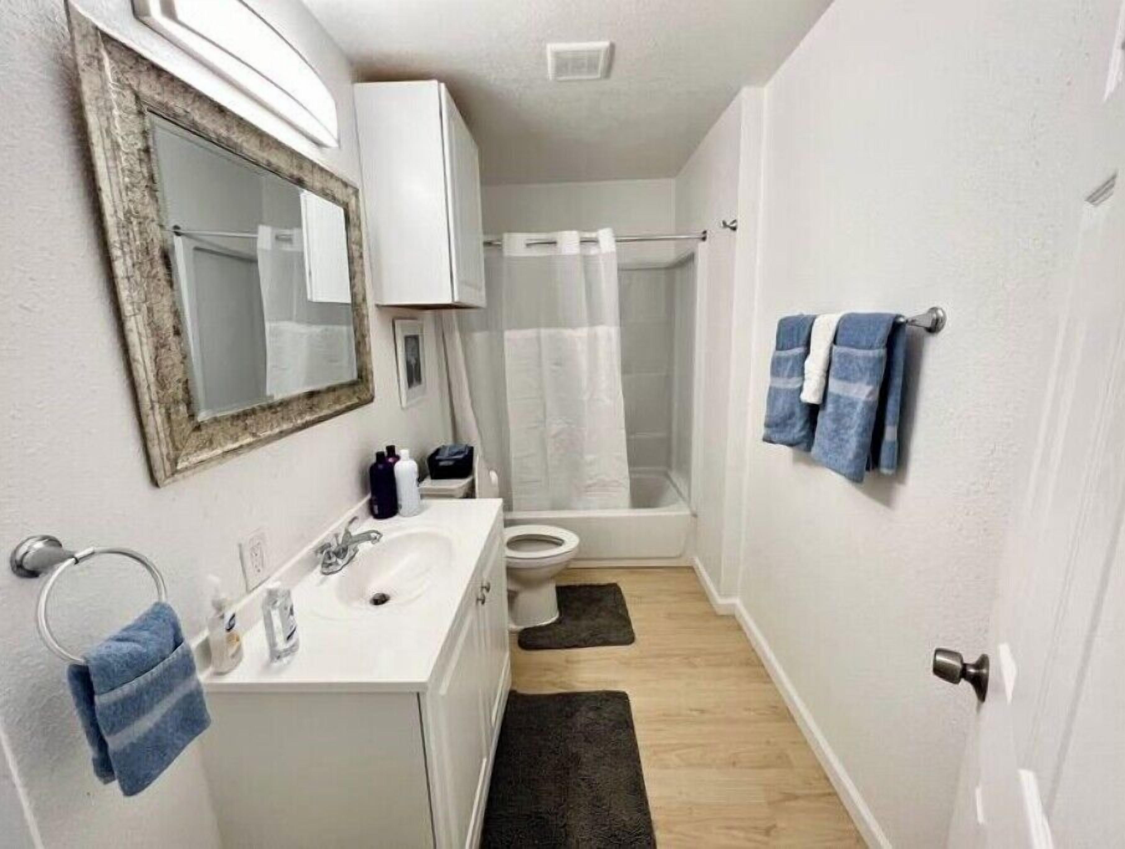 A small bathroom with a white sink, mirror, and toilet. There is a shower curtain and a towel rack with towels.