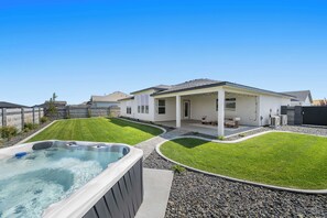 Ein modernes Haus mit Whirlpool, überdachter Terrasse und gepflegtem Rasen.