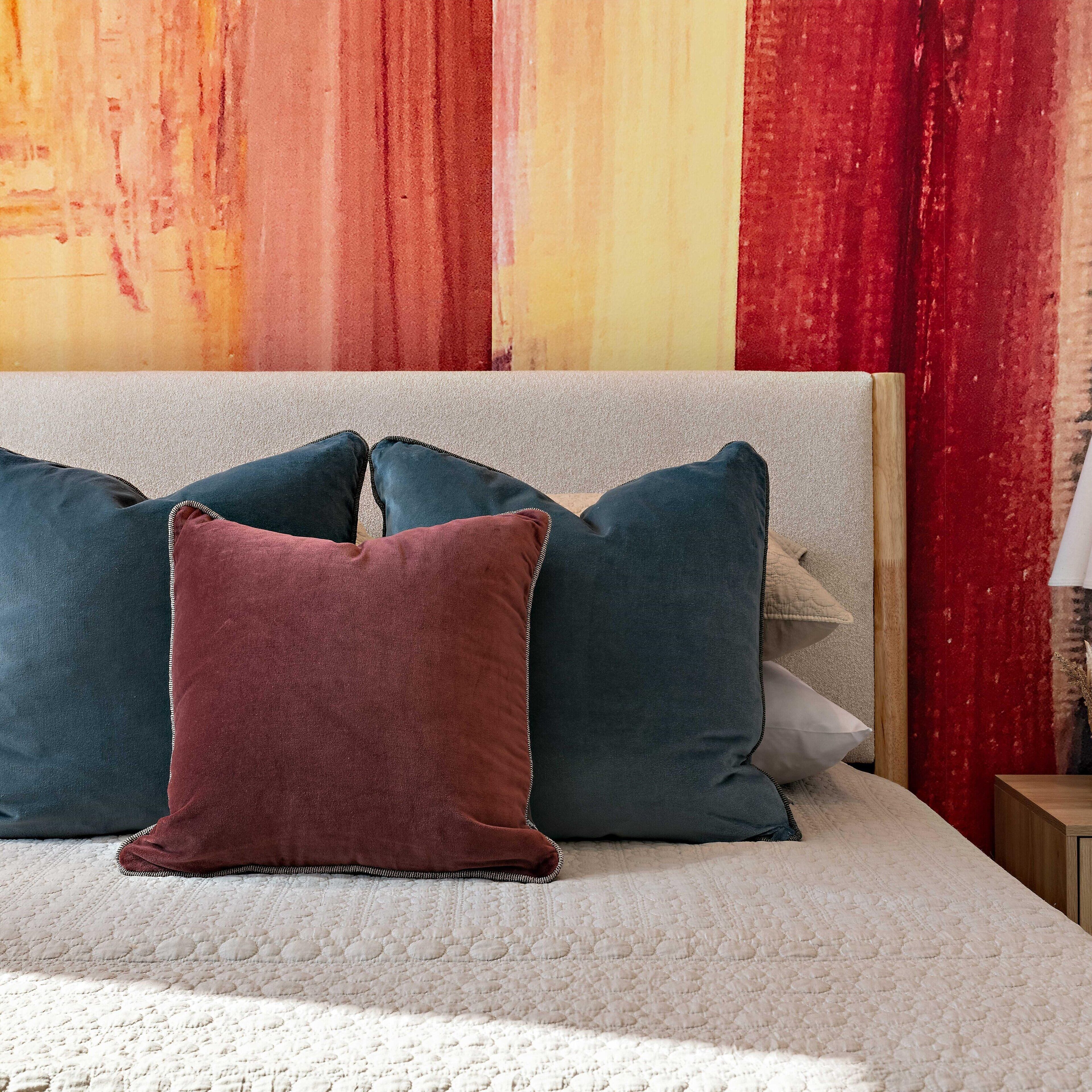 A bed with a white quilted cover and three pillows in different colors.