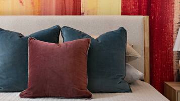 A bed with a white quilted cover and three pillows in different colors.