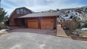 Una cabaña de madera con un amplio garaje, un porche cubierto y una terraza de madera.