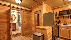 Una cocina compacta con paredes de madera, un refrigerador de acero inoxidable, un microondas y un lavamanos.