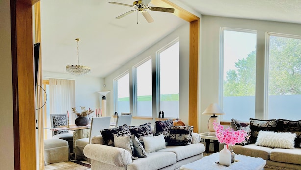 Ein geräumiges Wohnzimmer mit zwei Sofas, einem Couchtisch und einer Deckenleuchte. Große Fenster sorgen für viel Tageslicht.