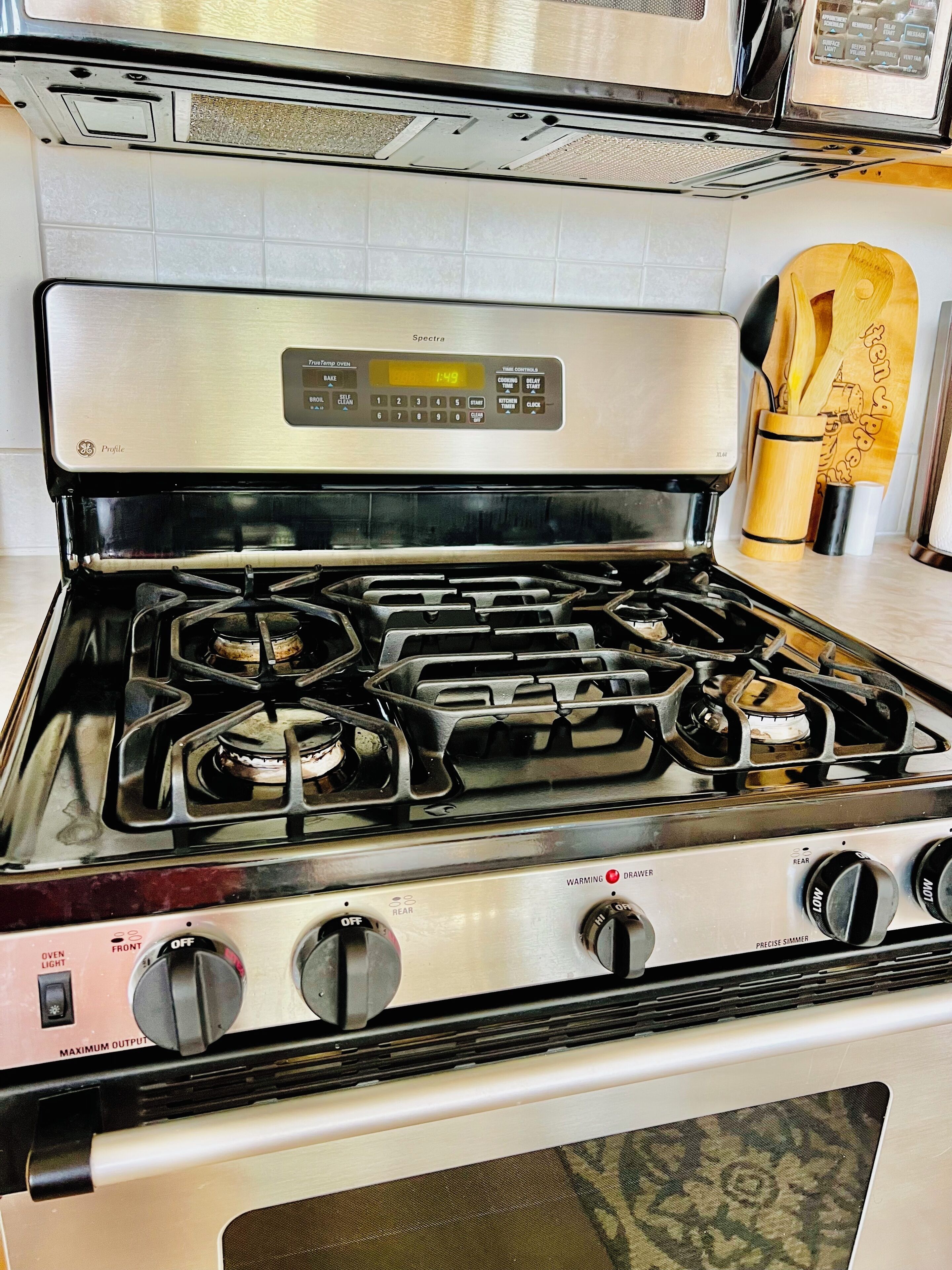 Een keuken met een roestvrijstalen fornuis, een magnetron erboven en een houten keukenhouders voor bestek op het aanrecht.