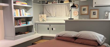 A bedroom with a bed, a bookshelf, a desk, and an air conditioning unit.