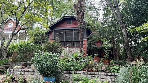 A house with a brick exterior and large windows, surrounded by lush greenery and a stone wall. - Decatur Garden Studio Apartment (Decatur)