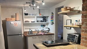 A compact kitchen with a refrigerator, stove, and various kitchen items on shelves. - Decatur Garden Studio Apartment (Decatur)