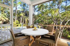 Un espacio al aire libre cubierto con mobiliario de mimbre, una mesa redonda y vistas a una piscina y árboles.