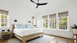 Ein Schlafzimmer mit einem hölzernen Bett, weißen Wänden und großen Fenstern mit Vorhängen.