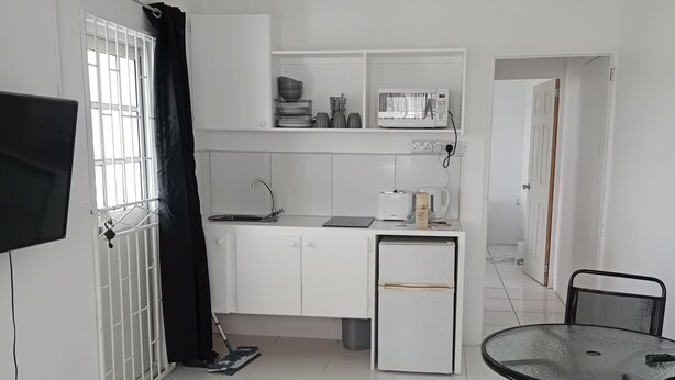 A compact kitchen with white cabinets, a microwave, a sink, and a small refrigerator. There's a dining table with chairs and a TV mounted on the wall. - Charming One-Bedroom Apartment in Peaceful Telescope, St. Andrews, Grenada (Telescope)