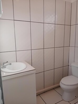 Une salle de bain avec un lavabo blanc, des toilettes et des murs carrelés.