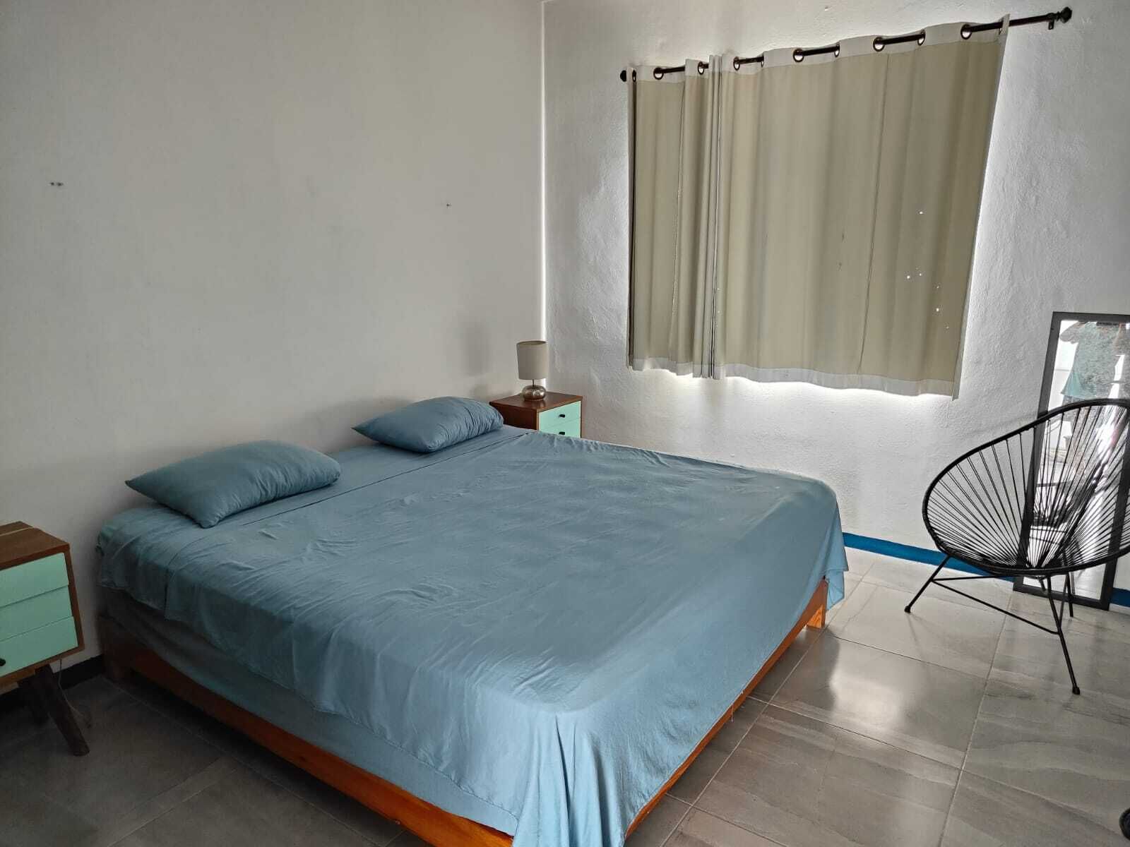 Une chambre à coucher avec un lit, une table de chevet, une chaise et une fenêtre avec des rideaux.