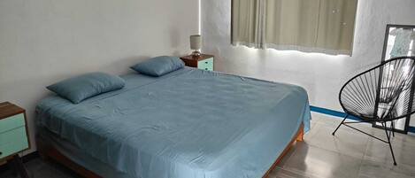 Une chambre à coucher avec un lit, une table de chevet, une chaise et une fenêtre avec des rideaux.
