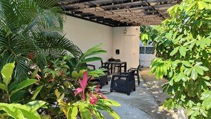 A covered patio area with outdoor furniture, surrounded by lush greenery and a concrete path. - Beautiful house for rent, walking distance to the beach 1 bedroom plus sofabed (Playa del Carmen)