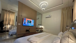 A modern hotel room with a large bed, a TV mounted on the wall, a mirror, and a bedside table with a lamp.